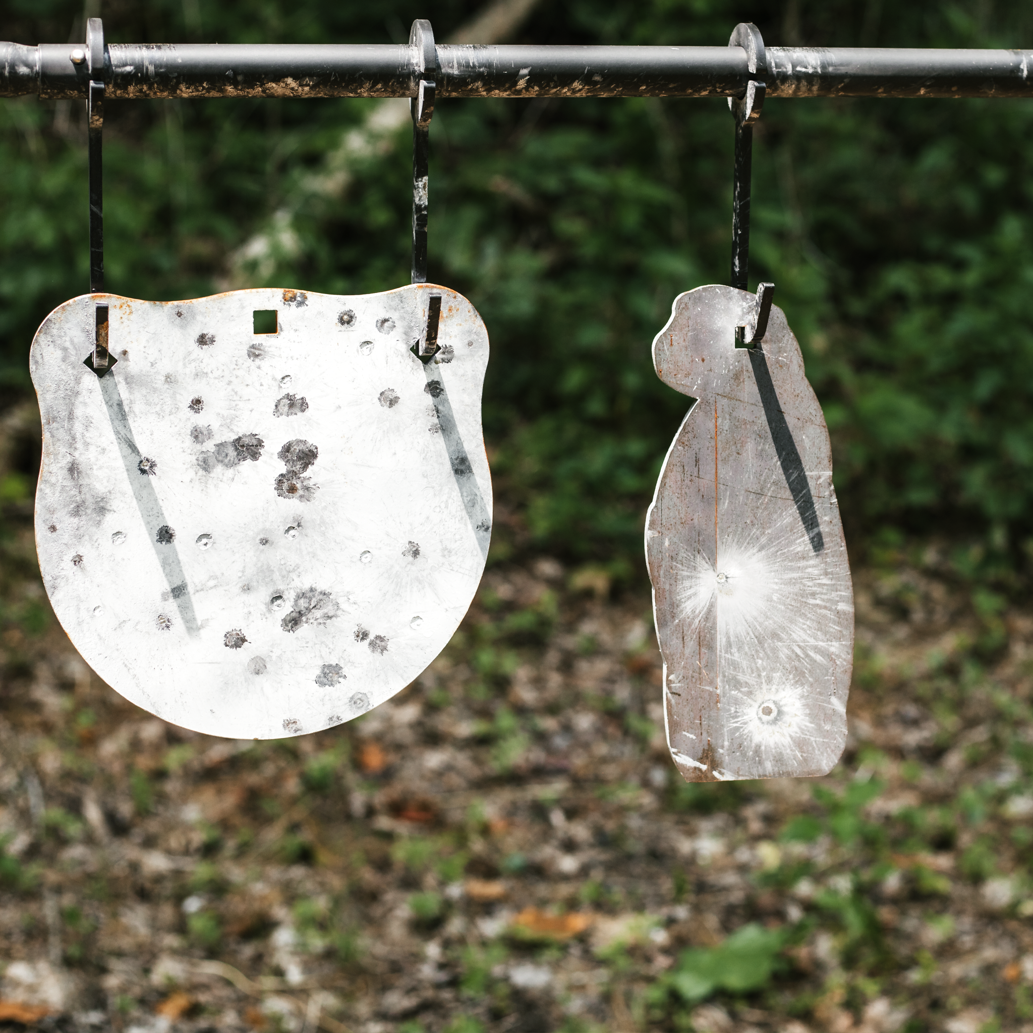 Raw prairie dog steel target hanging on a hook off of a conduit stand, also pictured is a painted gong