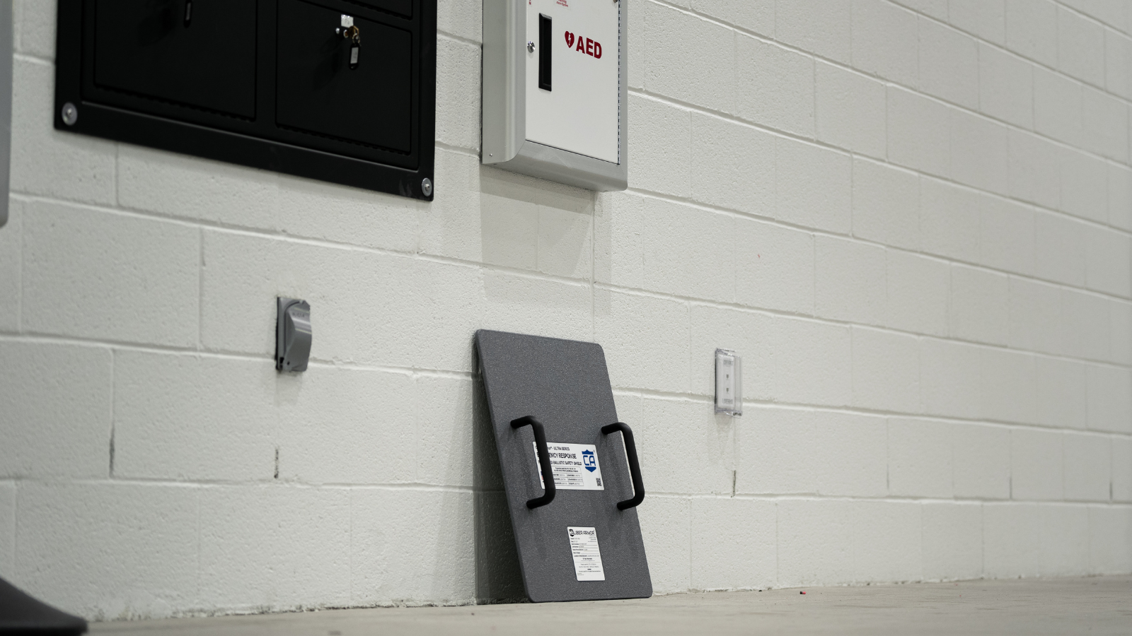 Level IIIA Ballistic shield against a white brick wall placed next to AED & other emergency response or active shooter protective gear
