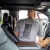 Man getting ready to deploy his CaliberX Core Ballistic Vehicle seat shield from behind where he sits in his vehicle, man is grabbing the soft handle of the shield