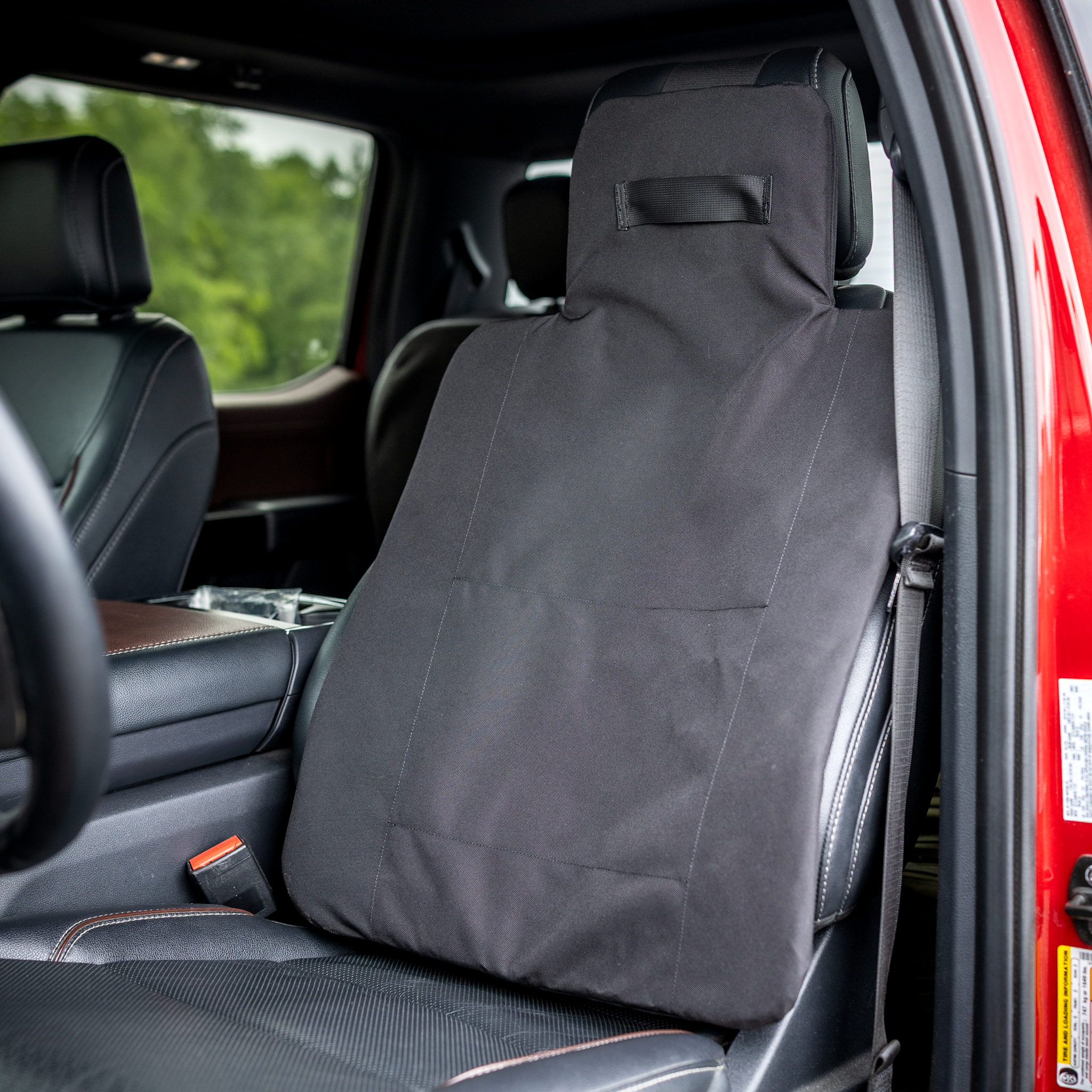 Black CaliberX Core Rapid Deployment Ballistic Vehicle seat shield installed on the driver's seat in a red truck with black interior