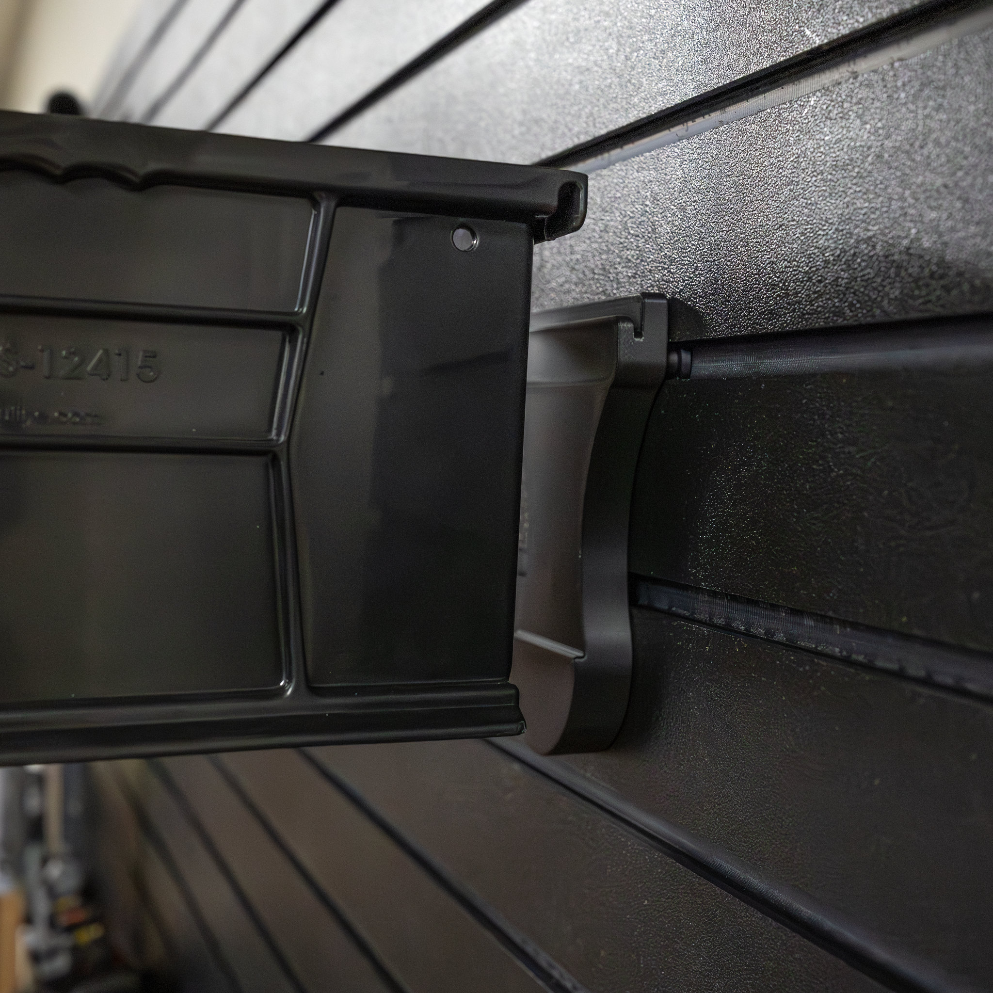 Close-up of how a plastic stackable utility storacy bin mounts to the Assault Wall Stackable Storage Bin Mount, shown mounted on a black Assault Wall tactical slat wall panel