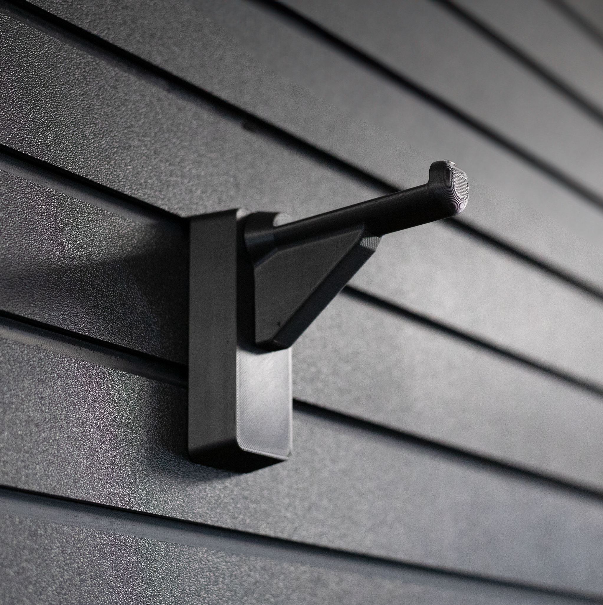 black plastic hanger for compound bows and crossbows shown mounted to a black tactical gear slat wall named Assault Wall