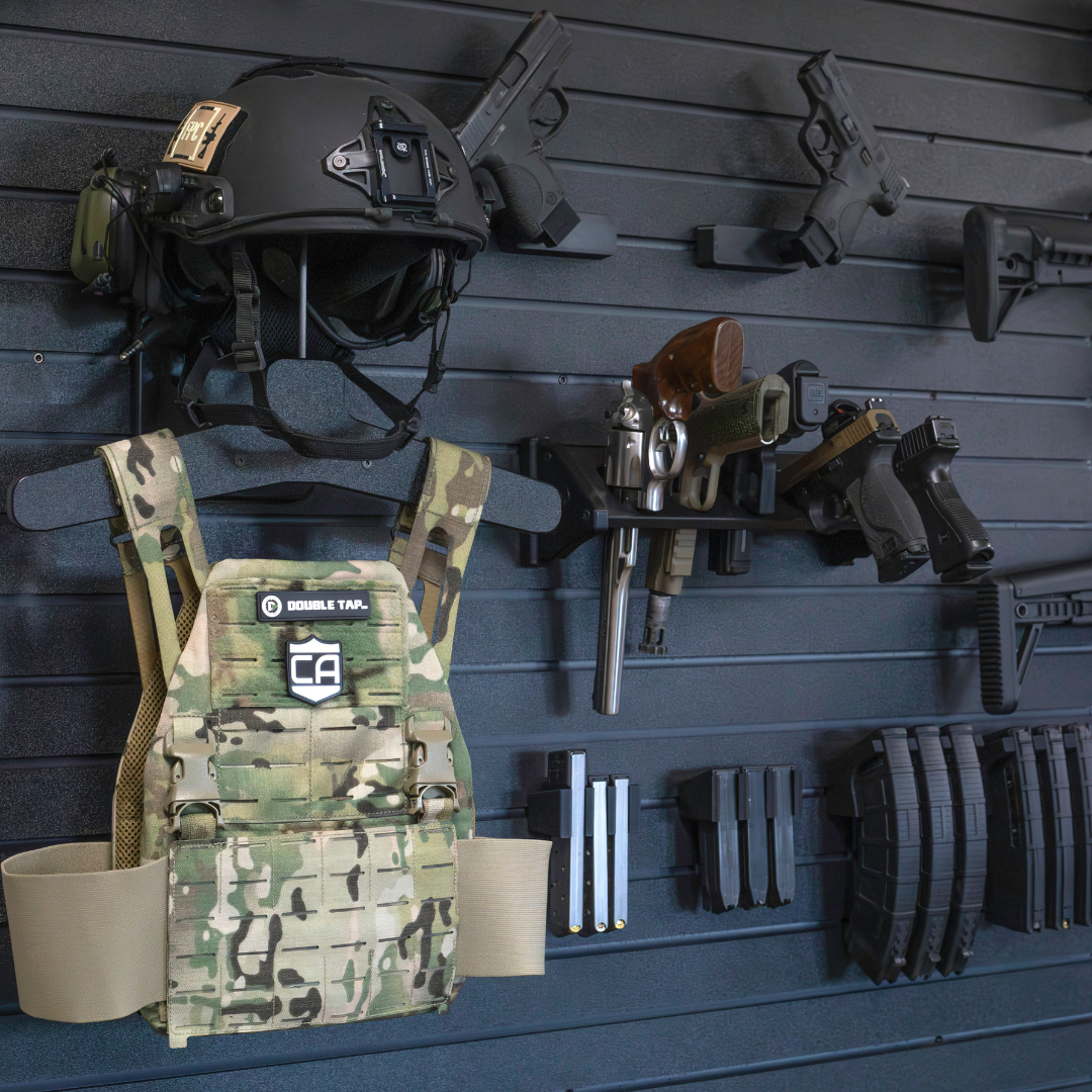 Tactical gear including a helmet, vest, magazines, and weapons mounted on the Assault Wall tactical slat wall panel wall system.