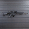 Right facing AR-15 rifle mounted by its magazine well on a black Assault wall slat wall panel