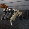 Black plastic five pistol storage mount loaded with smith and weston, revolver and glock pistols , all five pistols are resting in equally spaced slots, some with the pistol grip facing out and outhers with the grip facing up, mount is hanging from black tactical slat wall