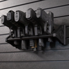 Black plastic five pistol storage mount loaded with smith and weston and glock pistols , all five pistols are resting in equally spaced slots, mount is hanging from black tactical slat wall