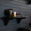 15" black plastic shelf with two support backets mounted on a black tactical slat wall, shelf has muffs, ammunition boxes, and a pistol magazine, shelf is mounted on a Assault Wall tactical slat wall.