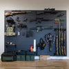 Assault Wall systems, black plastic wall-mounted slat wall display of various firearms and tactical gear in a room with wooden flooring.