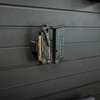 closer up side view image of Assault Wall Magnetic tactical gear mount shown with pistol mag and multi-tool mounted vertically by built in magnets, positioned on a black Assault Wall slat panel