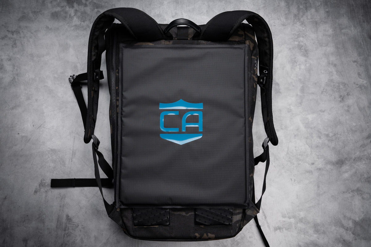 Lifestyle image of caliberx-iiia soft body armor rectangle laying on top of compatible backpack on a grey background
