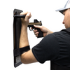 Person holding up a black 8" x 17" Caliber Armor Ballistic Shield with handle padded armrest & forearm strap while pointing a pistol