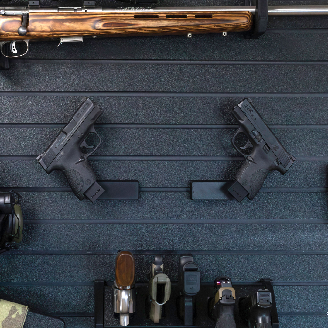 Left & Right facing black plastic caliber specific mag mounted pistol hangers installed on Assault Wall Tactical slat wall showcasing the adjustable mounting angles and directional mounts. 