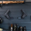 Left & Right facing black plastic caliber specific mag mounted pistol hangers installed on Assault Wall Tactical slat wall showcasing the adjustable mounting angles and directional mounts. 