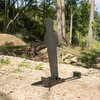 Angled view of AR500 fall popper with black metal base & inluded rubber bumper for forward or rear falling with a 42 inch uspsa popper target in wooded surroundings