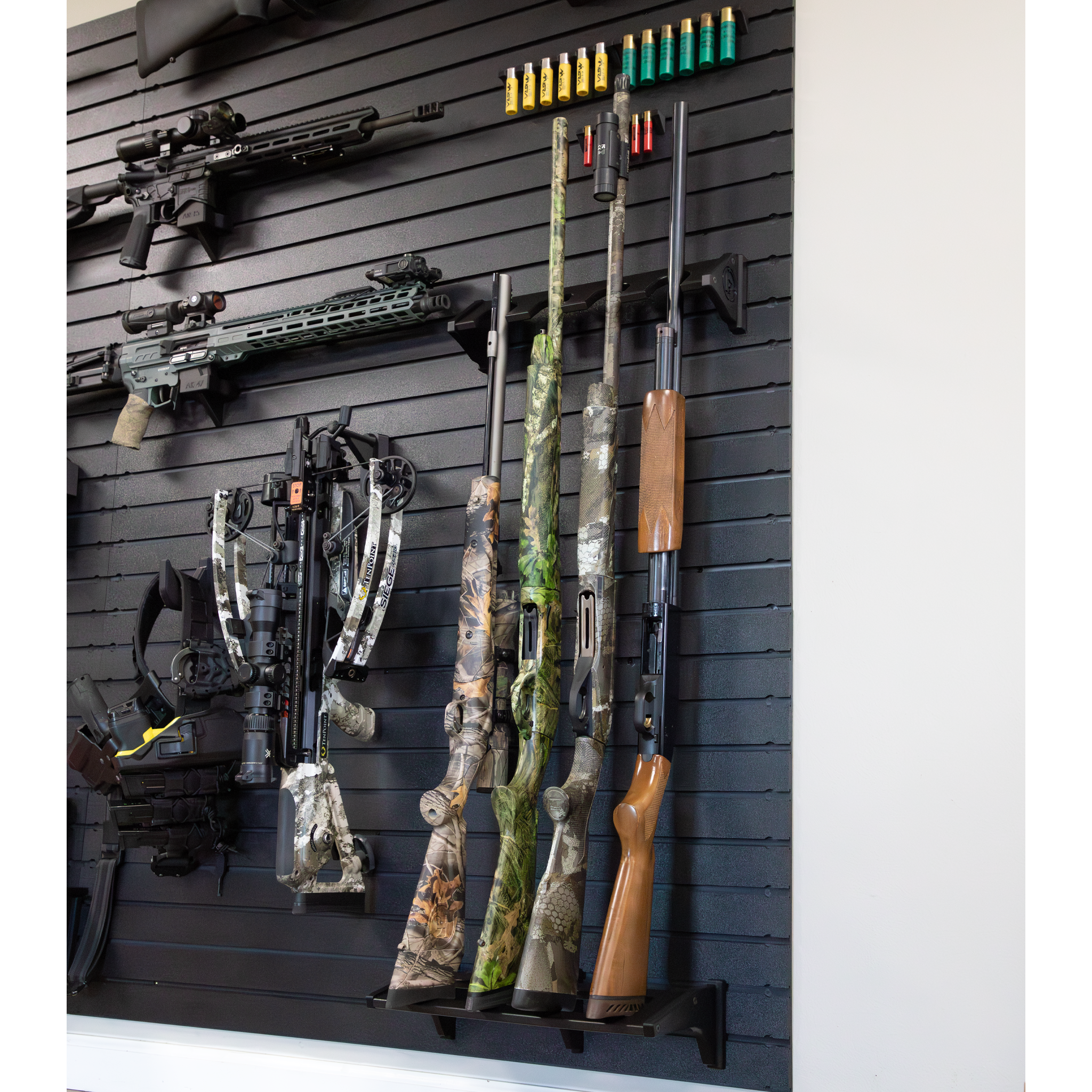 Black plastic vertical four gun storage mount, both upper & lower portion of mount shown mounted to our black  Assault Wall slat wall paneling loaded with shotguns & muzzelloaders with other tactical gear and guns shown mounted surrounding the mount